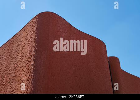 Red brown wavy brick wall of modern architecture with light and shadow under a blue sky in summer. Stock Photo