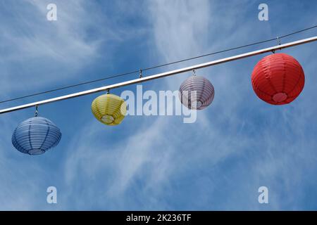 Blue, yellow and red lampion or latern lamps hanging on a line against a blue sky with small clouds. Stock Photo