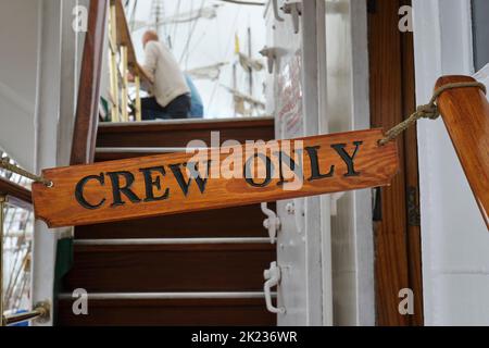 Wooden crew only sign on a ship against a blurred background with stairs and people. Stock Photo