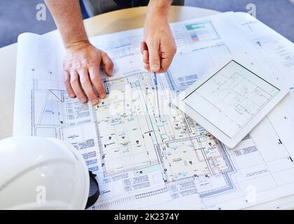 Looking for the smallest miscalculation. an architects hands examining blueprints and using a digital tablet. Stock Photo
