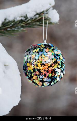 Hanging multi colored glitter Christmas ball on spruce and over blurred background Stock Photo