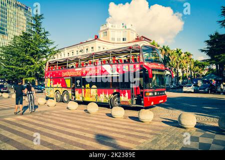 Batumi, Georgia - 4th august, 2022: tourist walk in street by red two floor double-decker classic sightseeing bus around city. Famous city attraction Stock Photo