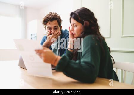 A young married couple is worried looking at the electricity bill or the arrival of very expensive taxes - lifestyle concept on the contemporary famil Stock Photo