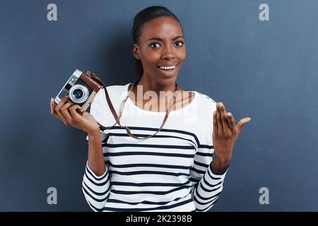 Shes got a snappy personality. Portrait of an attractive young woman holding a vintage camera on a gray backgorund. Stock Photo