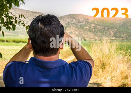 Happy New Year 2023 concept. Man watching transition from 2022 to new year 2023 text on sky. High resolution photo for large displays, print, banners. Stock Photo