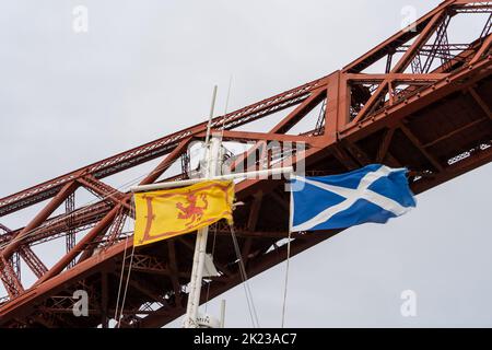 Two flags of Scotland - The Saltire and the Royal Banner of Scotland on a boat going under the Forth Rail Bridge in Scotland, UK Stock Photo