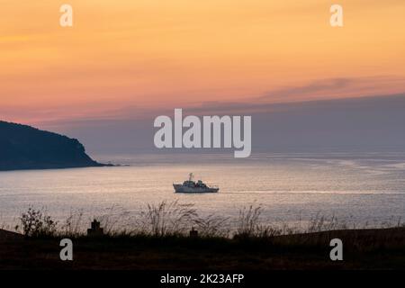 Superb landscape at sunset with a boat, isolated, close to the mainland, in a bay. Orange and purple coloured sky. Reflections of the sky on the water Stock Photo