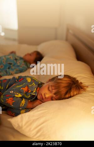 Tuckered out after a day full of fun. two little boys sleeping on a bed with the light on. Stock Photo