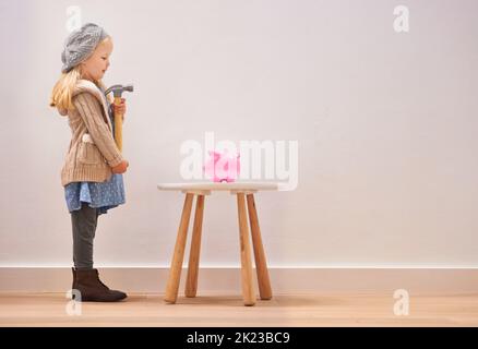 To break or not to break. A little girl standing in front of her piggy bank with a hammer. Stock Photo