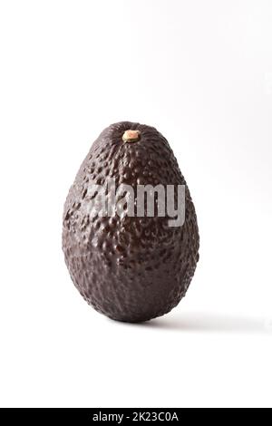 Detail of whole ripe avocado textured on white table and white isolated background.  Vertical composition. Stock Photo