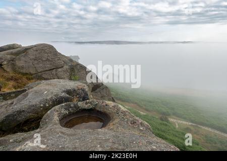 A cloud inversion in Wharfedale leads to a mist filled valley and an atmospheric view of the Cow and Calf Rocks on Ilkley Moor, West Yorkshire, Englan Stock Photo