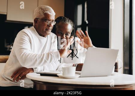 Senior couple waving their hands during a video call in their home. Mature couple having a virtual meeting with a retirement consultant. Ethnic senior Stock Photo