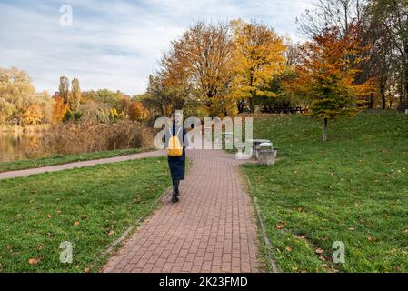 A young woman walks along a footpath in a park in the fall Stock Photo