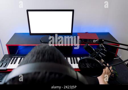 rear overhead view of man with headphones, looking at the computer monitor and with one hand on the mouse, working in his music studio. Stock Photo
