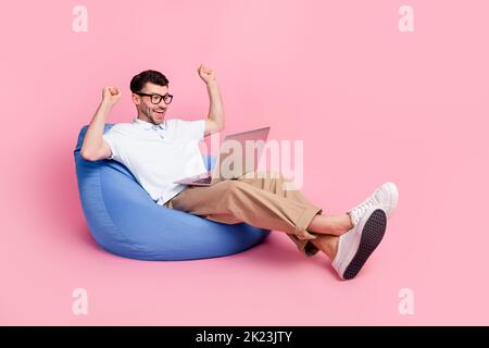 Full length photo of overjoyed man sitting cozy armchair rejoice success achievement empty space isolated on pink color background Stock Photo