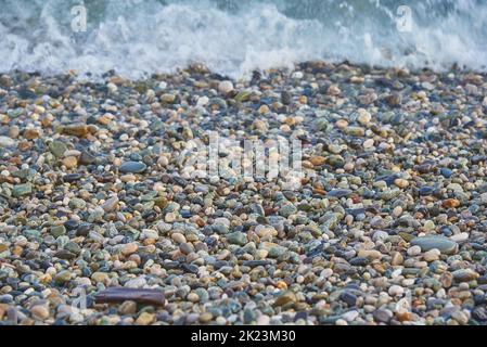 Small multicolored sea pebbles washed by a wave. Stock Photo