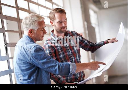 Is this where you want the window. two male architects discussing blueprints while standing indoors. Stock Photo