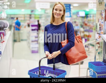Theres more to a pharmacy than medicine. Portrait of an attractive young woman standing with a basket in a pharmacy. Stock Photo