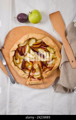 Homemade galette with apple and plum on a white linen tablecloth. Open pie. Top view of homemade pie crust on the table. rustic home baked fruit pie. Stock Photo