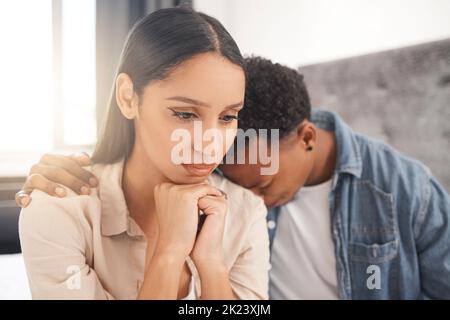 Upset couple fighting, arguing or breaking up while sitting on their bed in the bedroom at home. Sad man crying on the shoulder of his thinking wife Stock Photo