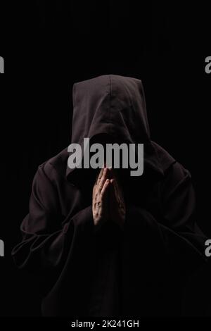 monk in hooded robe with praying hands and obscured face isolated on black,stock image Stock Photo