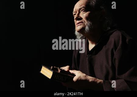 bearded monk in cassock holding bible and crucifix while thinking isolated on black,stock image Stock Photo