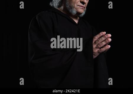 cropped view of bearded monk in cassock praying isolated on black,stock image Stock Photo