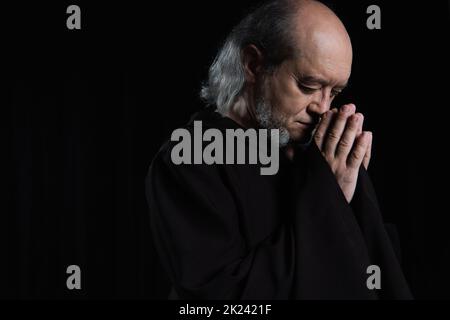 senior bearded monk in robe praying with closed eyes isolated on black,stock image Stock Photo