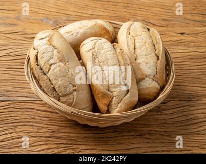 Whole grain french bread, salt bread or pistolet in a basket over wooden table. Stock Photo