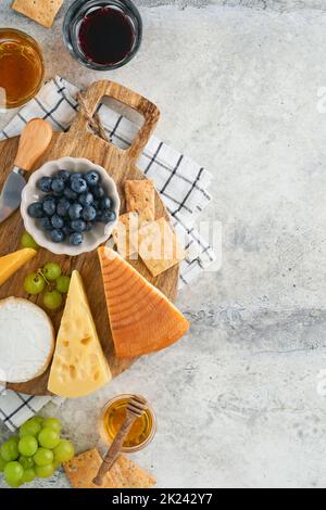 Assortment of cheese, honey, cracker, blueberries, grapes with red and white wine in glasses antipasto server on white marble board on grey background Stock Photo