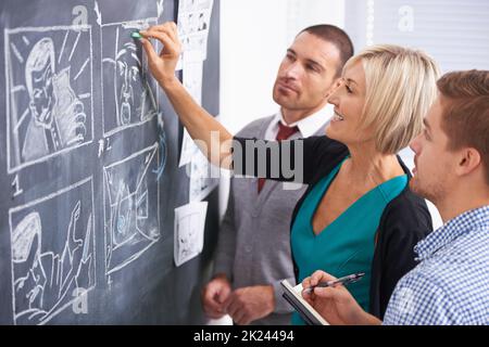 A team effort. A team of businesspeople drawing up a storyboard on a chalkboard in the office. Stock Photo