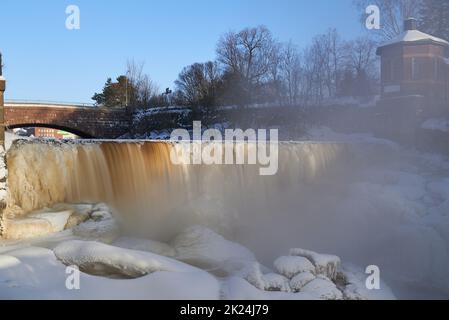 Helsinki, Finland - February 18, 2021: Water pours over frozen museum dam in the mouth of Vantaa River at the Vanhankaupunginkoski rapids (Vanhankaupu Stock Photo