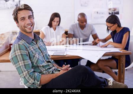 I love coming up with new designs. Portrait of a handsome male architect with his colleagues working in the background. Stock Photo