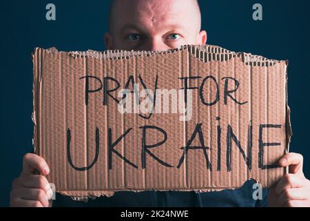 Man holding Pray for Ukraine banner. Concept symbol of help support and no war in the country of Ukraine. Stock Photo
