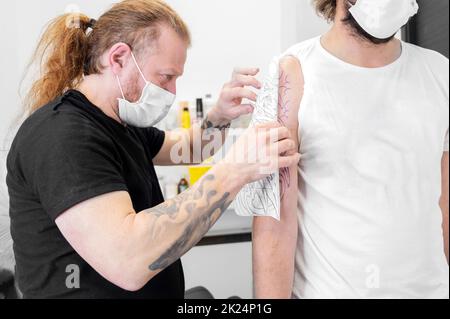 Skilled Tattoo artist putting a sketch on the arm of a man. High quality photo Stock Photo