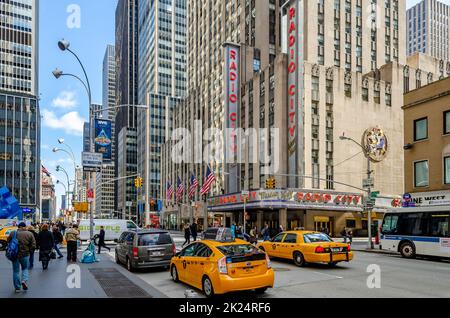 Radio City Music Hall, New York City with two yellow Taxi Cabs and traffic in the forefront, people walking on the sidewalk during daytime, horizontal Stock Photo