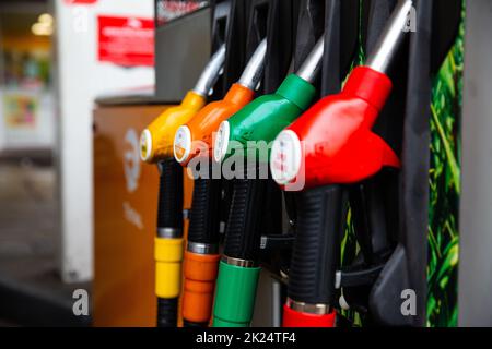 Close up on fuel nozzle in oil dispenser with gasoline and diesel in service gas station. Blue, green, red, golden colors. Stock Photo
