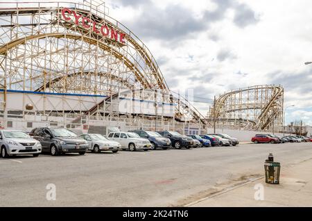 Cyclone Wooden Rollercoaster at Luna Park Amusement Park, Coney island, Brooklyn, view from the side with lots of cars parked in front next to the str Stock Photo