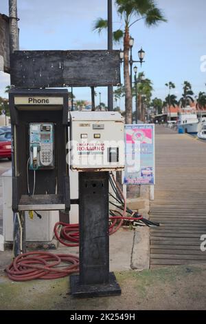 ORANJESTAD, ARUBA - DECEMBER 3, 2021: Old public phone and a box from Bells Technologies stating Cheaper Than Roaming, located along the Wind Creek Ma Stock Photo