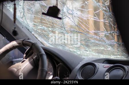 Broken windshield of a car from a bullet, from a shot from a firearm, view from the inside of the cabin. Damaged glass with traces of an oncoming ston Stock Photo