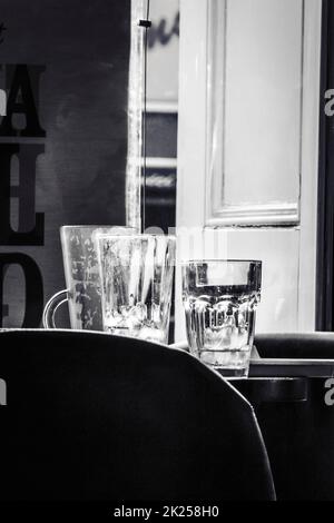 Empty glasses on a table backlit by a shuttered window Stock Photo