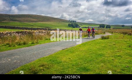 Three male cyclists socialising on bikes on a country lane over Malham Moor, Yorkshire Dales National Park, North Yorkshire, England, UK Stock Photo