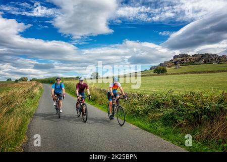 Three male cyclists socialising on bikes on a country lane with Almscliffe Crag behind, North Yorkshire, England, UK Stock Photo