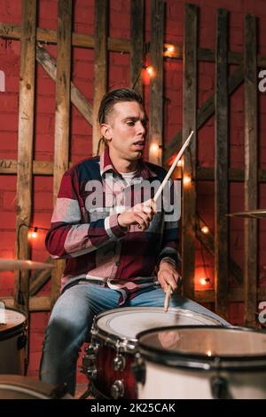 Adult male drummer playing music on drum set on stage decorated with glowing garland during live performance Stock Photo