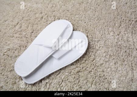 White slippers on grey mat. Pair of comfortable slippers in hotel room