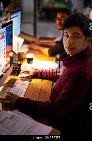 Getting the job done. a group of young coworkers working in a dimly-lit office. Stock Photo