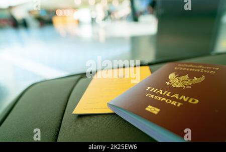Thailand passport and vaccine passport on baggage on blur background of tourist in the airport. Certificate of vaccination for travel during coronavirus outbreak. Thai words are Thailand passport. Stock Photo
