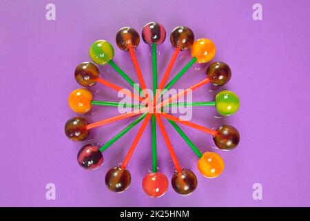 Various colorful lollipops on pastel background. Bright juicy colored lollipops on a lilac background. Lollipops in the form of a flower. Fruit candy Stock Photo
