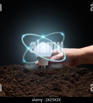 a female hand holds a white glowing light bulb over the ground. Concept of new ideas and innovations, start-up Stock Photo