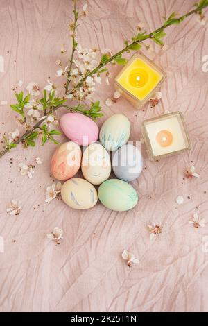 Beautiful watercolor paints on Easter eggs that lie on a delicate pink cloth along with burning candles. Easter concept. Stock Photo